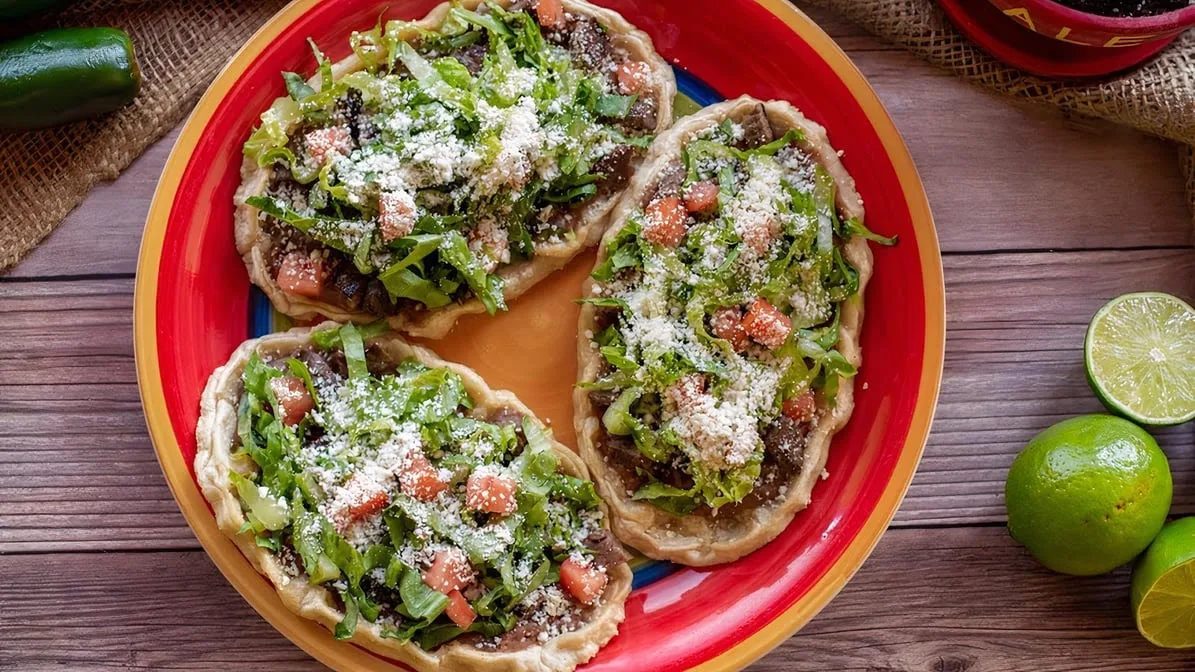 Sopes topped with meat, lettuce, tomato and cotija cheese